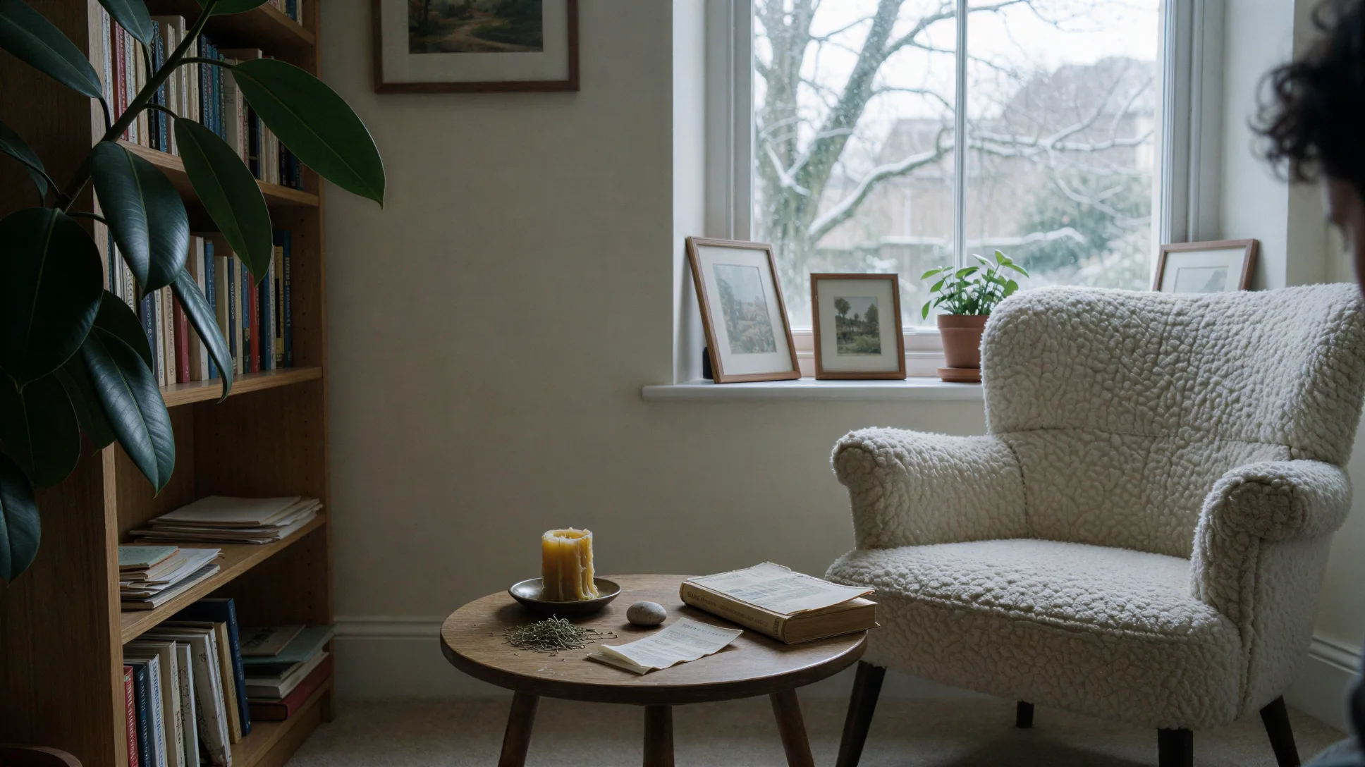 A reading chair beside books, a candle and a winter window